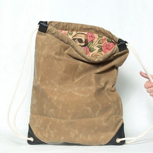 May include: A brown canvas drawstring bag with black leather accents and white drawstrings. The bag is open, revealing a floral print lining with a skull design.
