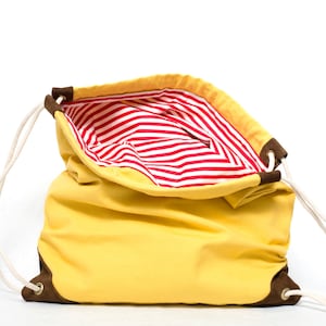 Puede incluir: Una bolsa de cordón amarilla con un forro de rayas rojas y blancas. La bolsa está abierta y el forro es visible.