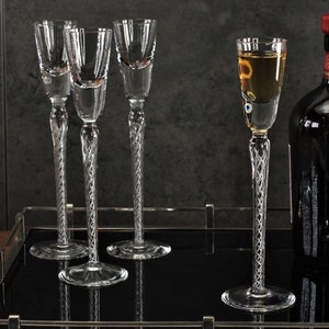 Könnte beinhalten: Ein silbernes Serviertablett mit vier klaren Schnapsgläsern aus Glas und einer Flasche Drambuie-Likör. Das Tablett hat eine schwarze Oberfläche und silberne Griffe.