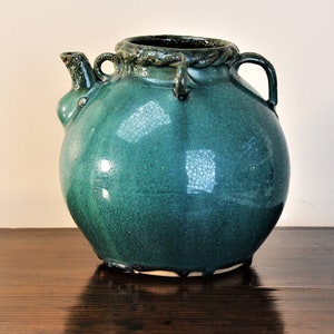 May include: A teal ceramic jug with a rounded body and a spout. The jug has two handles and a textured rim.