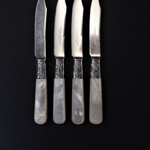 May include: Four silver butter knives with mother-of-pearl handles. The knives have a decorative design on the handle and the words "LAIDLAW BROTHERS & CO. SHEFFIELD" are engraved on the blade.
