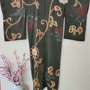 May include: A green silk kimono with a floral pattern in shades of brown, gold, and white. The kimono has a traditional Japanese design with a long, flowing silhouette.