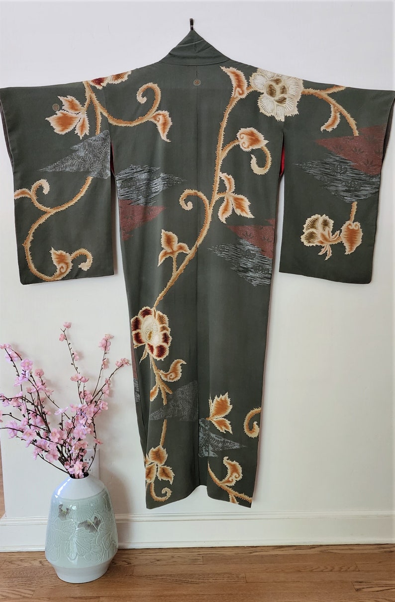 May include: A green silk kimono with a floral pattern in shades of brown, gold, and white. The kimono has a traditional Japanese design with a long, flowing silhouette.