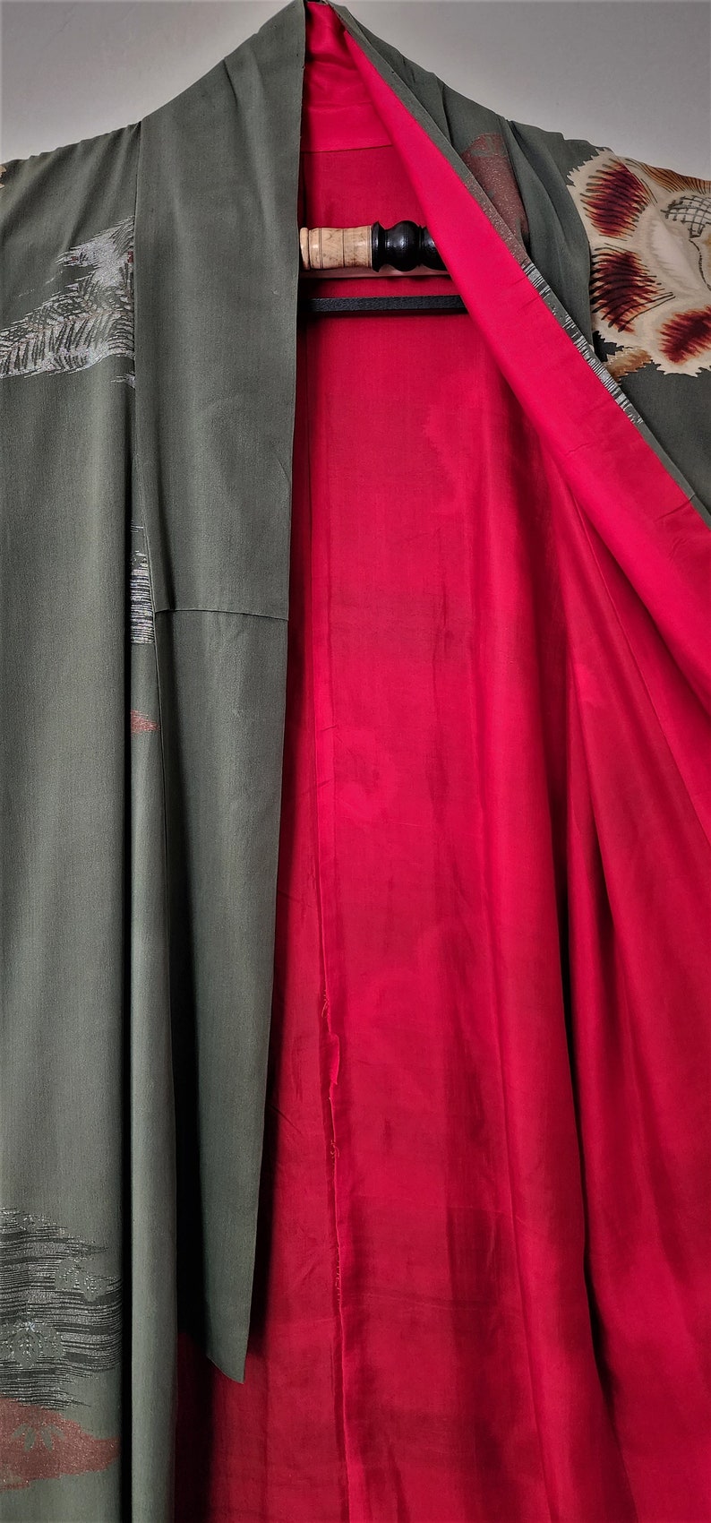 May include: A green kimono with a red lining. The kimono has a floral pattern on the sleeve and a geometric pattern on the front.