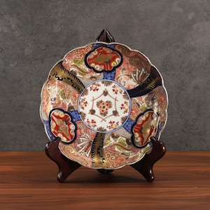 May include: A decorative ceramic plate with a blue, red, gold, and white floral pattern. The plate is on a wooden stand.