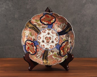 May include: A decorative ceramic plate with a blue, red, gold, and white floral pattern. The plate is on a wooden stand.