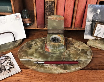 Op de afbeelding: Een groene onyx bureauset met een pennenhouder, inktpot en een brievenhouder. De set staat op een houten bureau met een kalender, een ansichtkaart en een bril.