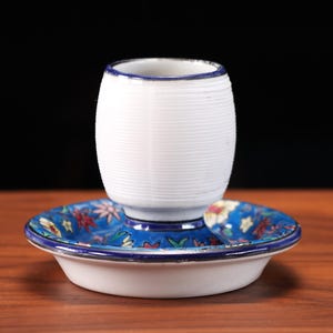 May include: A white ceramic match holder with a blue floral design on the base. The holder has a ribbed texture and a blue rim. The base is a small dish with a matching floral pattern.