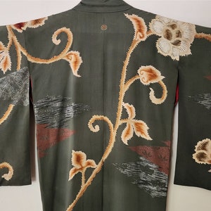 May include: A green kimono with a floral pattern in shades of brown and white. The kimono has a traditional Japanese design with a large flower on the back and smaller flowers on the sleeves.