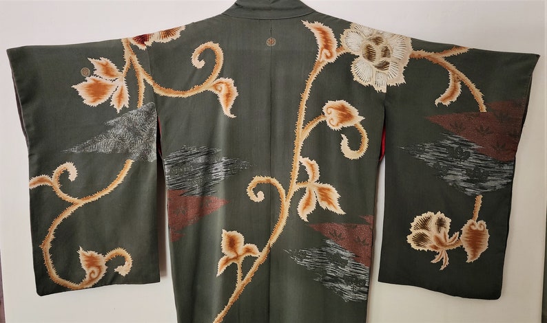 May include: A green kimono with a floral pattern in shades of brown and white. The kimono has a traditional Japanese design with a large flower on the back and smaller flowers on the sleeves.