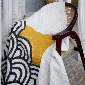 Peut inclure: Une chaise en bois fonc&eacute; avec un dossier en cannage et un coussin d'assise vert clair, recouverte d'une courtepointe blanche orn&eacute;e d'un grand bloc jaune moutarde et de motifs de lignes arqu&eacute;es noires avec des surpiq&ucirc;res blanches visibles.