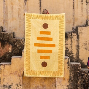 Puede incluir: Dos mujeres se paran frente a una tela amarilla y naranja con un patr&oacute;n que cuelga de una pared de piedra. La tela tiene un dise&ntilde;o geom&eacute;trico con c&iacute;rculos y rect&aacute;ngulos. Las mujeres visten ropa tradicional india.