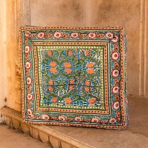 May include: A square floor cushion with a blue, green, orange, and red floral pattern. The cushion is sitting on a stone step.