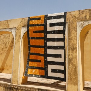 May include: A black and white patterned rug with a yellow and black geometric design hangs in a doorway of a yellow building.