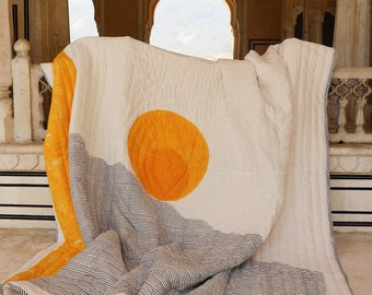 May include: A white and yellow striped cotton quilt with a large yellow circle in the centre. The quilt is folded and draped over a marble railing in a building with arched doorways.