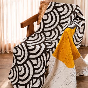 Peut inclure: Un jet&eacute; de lit matelass&eacute; pr&eacute;sentant un motif r&eacute;p&eacute;titif d'arcs noirs et blancs sur la majeure partie du tissu, avec une section jaune moutarde unie et une section blanche unie, le tout rehauss&eacute; par des d&eacute;tails de broderie au point droit.