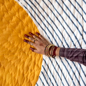 May include: A yellow and white striped quilt with a hand resting on the yellow section. The quilt is made of cotton and has a quilted design. The quilt is a traditional Indian design and is perfect for adding a touch of color and style to any room.