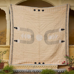 Może przedstawiać: Beige kołdra bawełniana z geometrycznym wzorem w kolorze czarnym. Kołdra jest powieszona na ścianie z kamiennym łukiem nad nią.