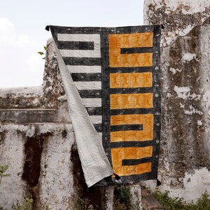 May include: A black and white striped fabric with a yellow and black geometric pattern hanging on a white wall. The fabric is folded in half and the yellow and black pattern is on the right side of the image.