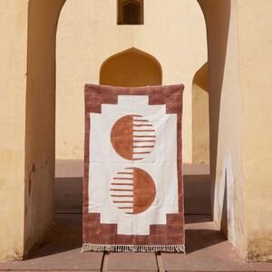 May include: A white and brown geometric rug with a repeating pattern of half circles. The rug is hanging in a doorway with a yellow archway.