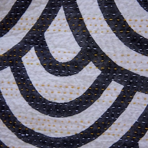 Peut inclure: Un textile pr&eacute;sentant un motif r&eacute;p&eacute;titif de formes courbes noires sur un fond blanc. Le tissu est orn&eacute; de rang&eacute;es de petits points de couture horizontaux en fil blanc et jaune moutarde, cr&eacute;ant un aspect textur&eacute; et matelass&eacute; sur la surface.