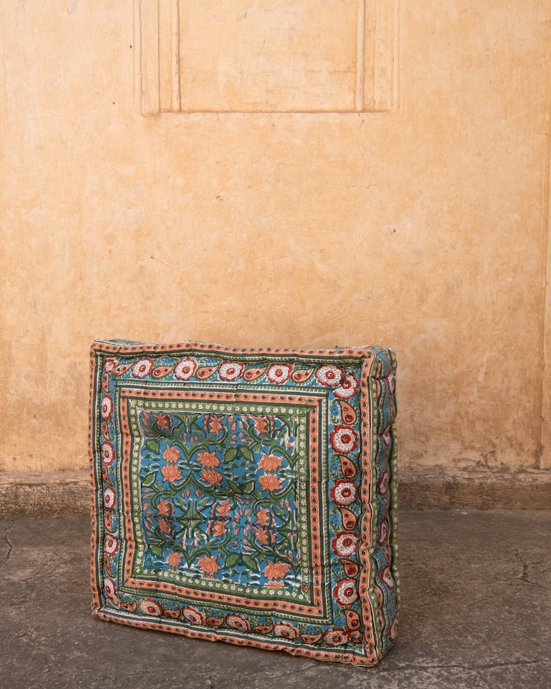 May include: A square floor cushion with a floral pattern in shades of green, pink, and blue. The cushion has a border with a paisley design.