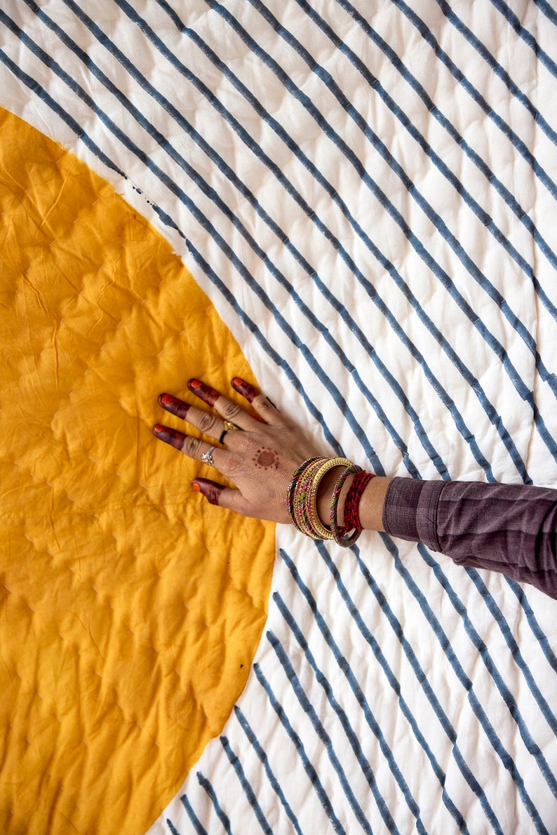 May include: A yellow and white striped quilt with a hand resting on the yellow section. The quilt is made of cotton and has a quilted design. The quilt is a traditional Indian design and is perfect for adding a touch of color and style to any room.