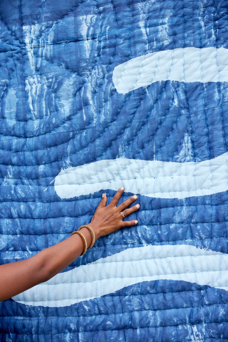 K&ouml;nnte beinhalten: Blau-wei&szlig; gesteppter Textil mit wellenartigem Muster. Die Steppdecke hat einen dunkelblauen Hintergrund mit helleren blauen und wei&szlig;en Akzenten. Die Textur ist sichtbar, mit gen&auml;hten Linien, die einen gesteppten Effekt erzeugen.