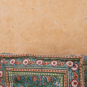 May include: A close-up of a colorful patterned cushion with a floral design. The cushion is made of fabric and has a light blue background with orange, green, and white accents.