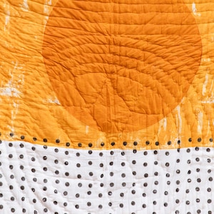 May include: A quilted fabric with a large orange circle in the top half and a white background with black polka dots in the bottom half.
