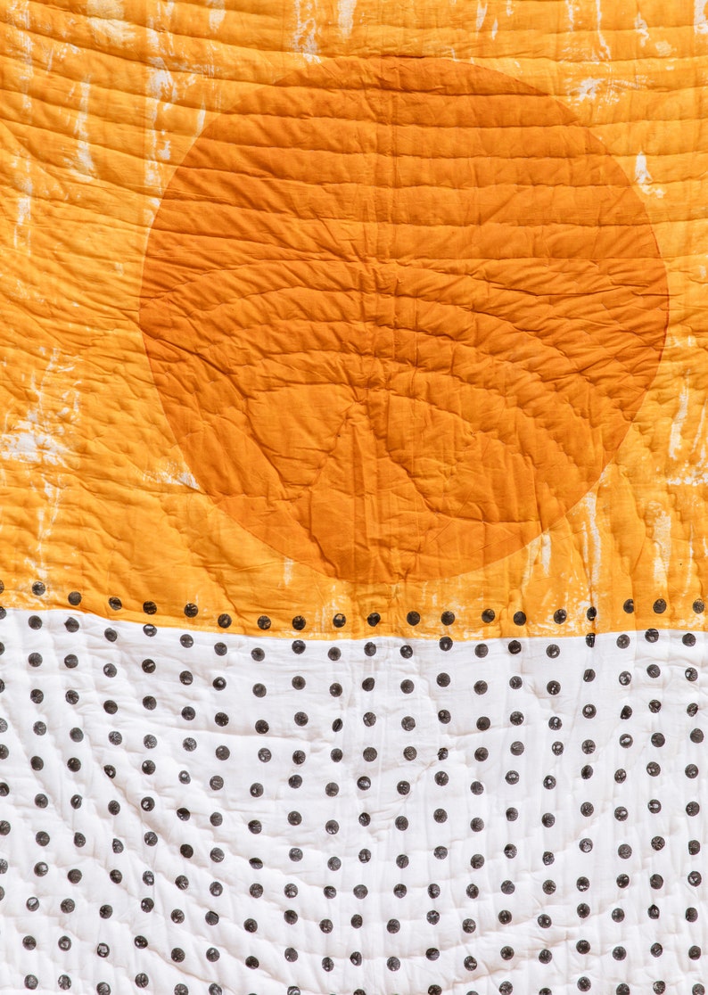 May include: A quilted fabric with a large orange circle in the top half and a white background with black polka dots in the bottom half.
