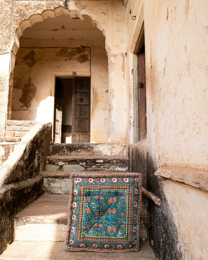 May include: A blue and orange patterned rug with floral designs sits on the steps of a weathered stone building.