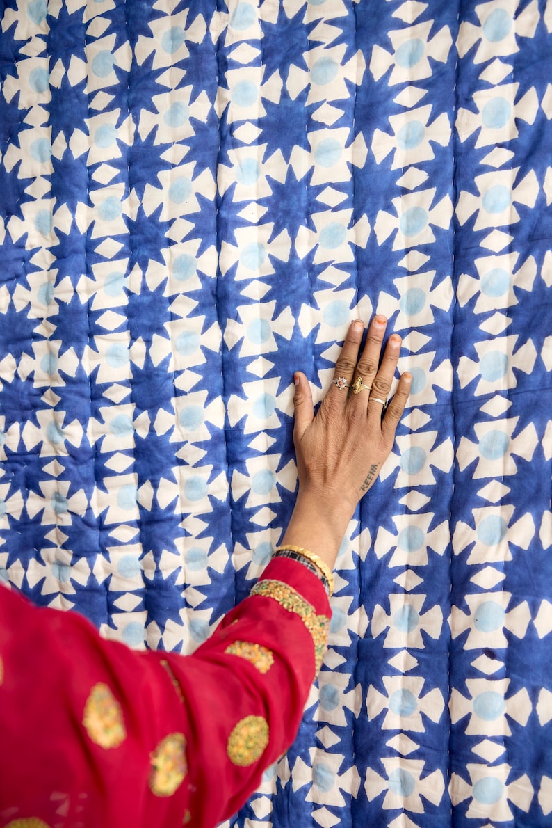May include: A blue and white patterned quilt with a repeating star design. The quilt is made of a soft fabric and has a quilted texture. The design is a mix of dark blue stars and light blue circles on a white background.