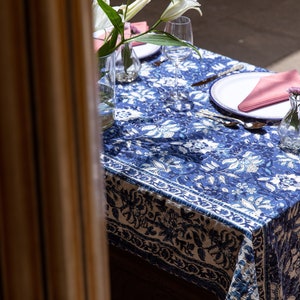 Puede incluir: Un mantel de mesa floral azul y blanco con una servilleta rosa y un plato blanco sobre una mesa. Hay dos jarrones de vidrio transparente con flores blancas y un jarr&oacute;n de vidrio transparente con flores rosas.