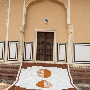May include: A white and brown quilt with a geometric pattern of two half circles. The quilt is laid out on the steps of a building with a brown door and white trim.