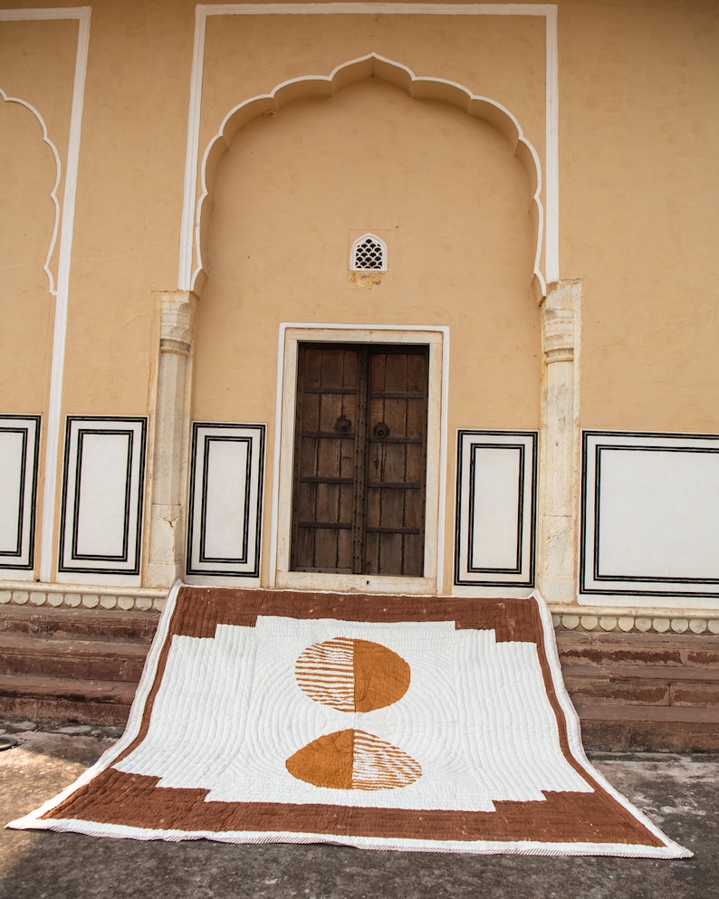 May include: A white and brown quilt with a geometric pattern of two half circles. The quilt is laid out on the steps of a building with a brown door and white trim.