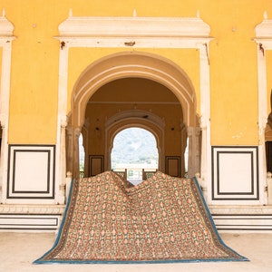 Pu&ograve; includere: Un tappeto colorato con motivi &egrave; drappeggiato su un arco in un edificio giallo con modanature bianche. Il tappeto ha un bordo blu e un motivo floreale.