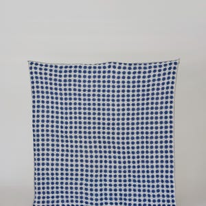 May include: A navy blue and white patterned blanket. The blanket features a repeating starburst design. The edges are finished with a simple, light-colored border. The blanket is displayed against a plain white background.