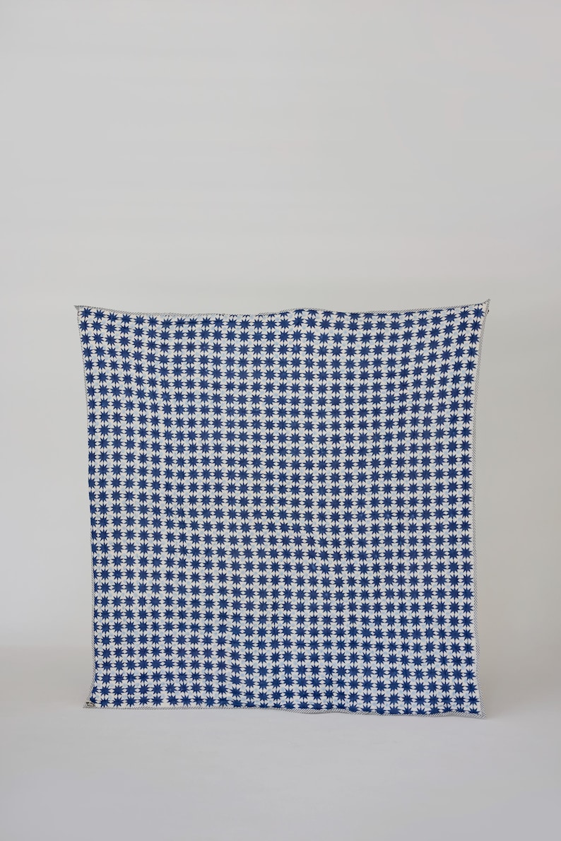 May include: A navy blue and white patterned blanket. The blanket features a repeating starburst design. The edges are finished with a simple, light-colored border. The blanket is displayed against a plain white background.