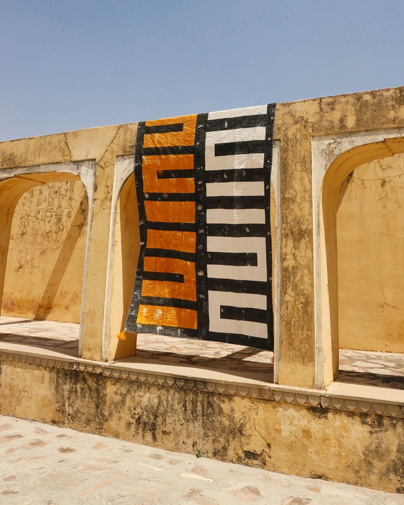 May include: A black and white patterned rug with a yellow and black geometric design hangs in a doorway of a yellow building.