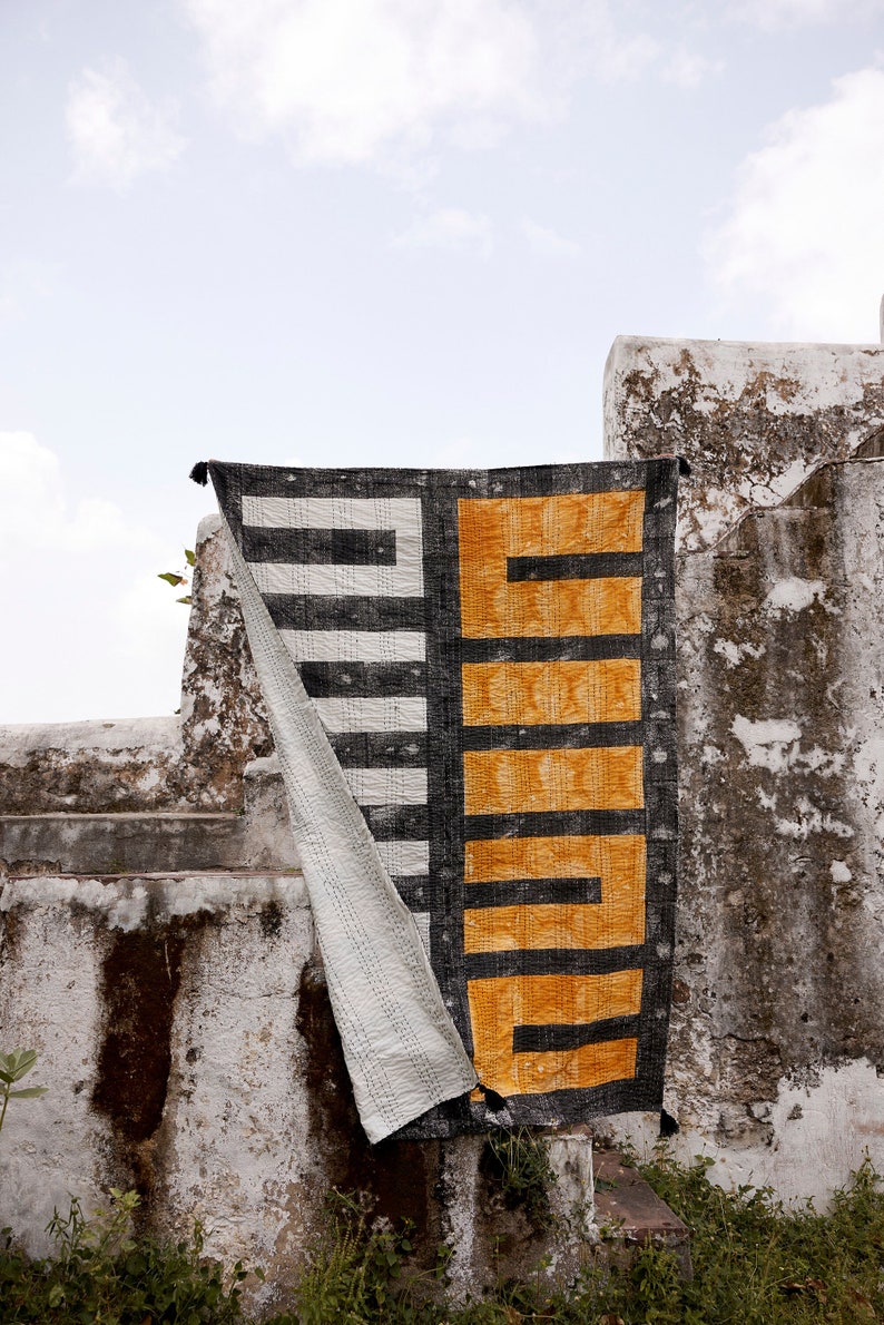 May include: A black and white striped fabric with a yellow and black geometric pattern hanging on a white wall. The fabric is folded in half and the yellow and black pattern is on the right side of the image.