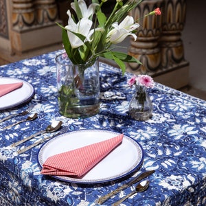 Puede incluir: Un mantel de mesa floral azul y blanco con un plato blanco y una servilleta a cuadros rojos. Un jarr&oacute;n con lirios blancos y un jarr&oacute;n peque&ntilde;o con flores rosas est&aacute;n sobre la mesa.