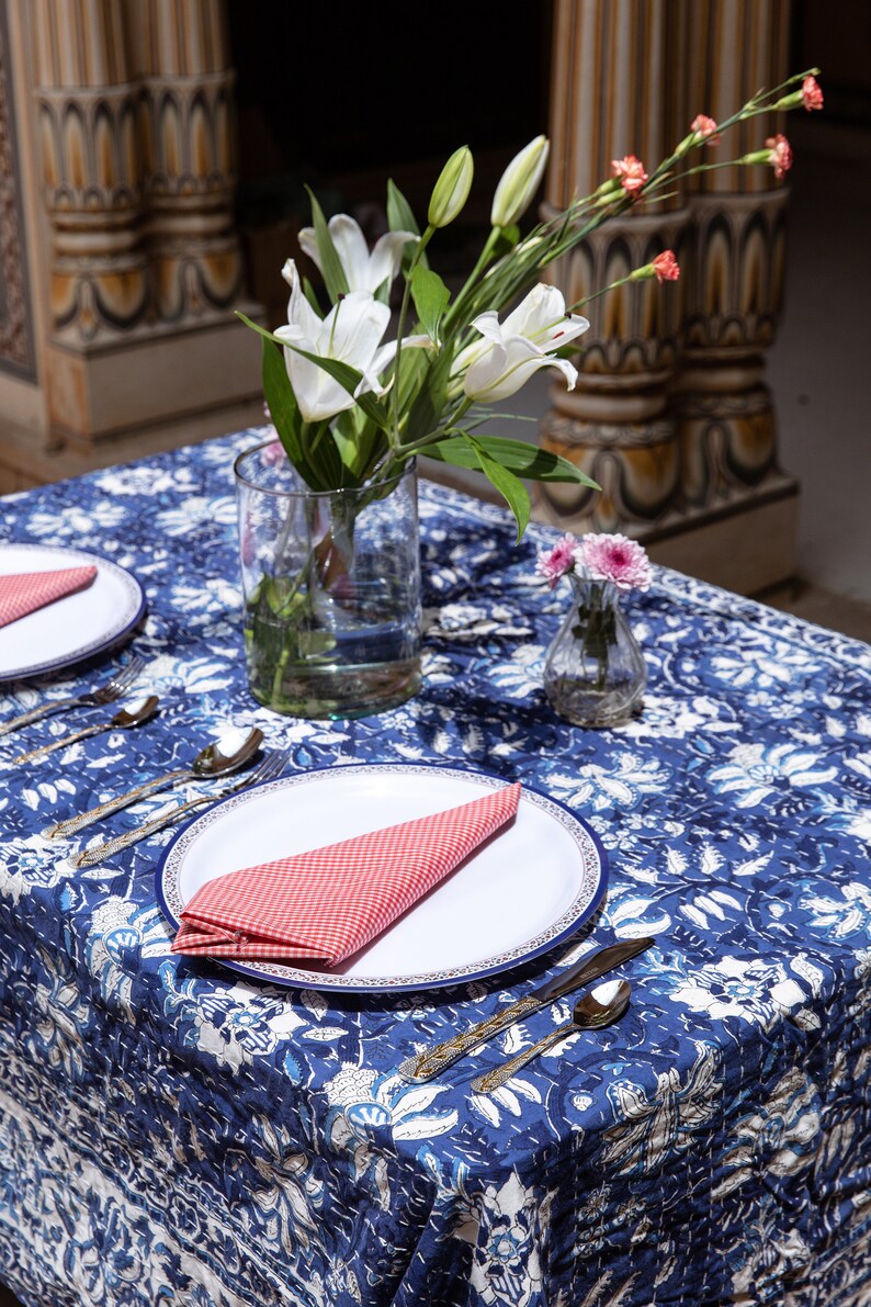 Puede incluir: Un mantel de mesa floral azul y blanco con un plato blanco y una servilleta a cuadros rojos. Un jarr&oacute;n con lirios blancos y un jarr&oacute;n peque&ntilde;o con flores rosas est&aacute;n sobre la mesa.