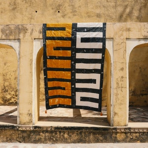 May include: A black and white geometric patterned fabric hanging in a doorway with a yellow and black geometric patterned fabric hanging next to it.