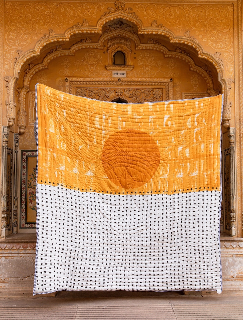 May include: A large yellow and white quilt with a sun design in the center. The quilt is hanging on a wall with a yellow background.