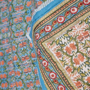 Puede incluir: Una colcha con estampado floral azul y naranja con un borde blanco. La colcha est&aacute; doblada por la mitad y el estampado es visible en ambos lados.