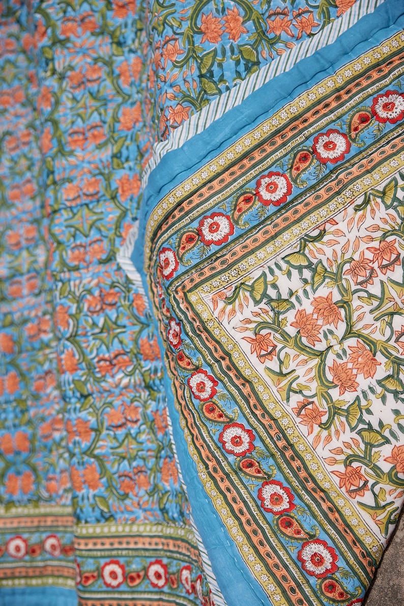Puede incluir: Una colcha con estampado floral azul y naranja con un borde blanco. La colcha est&aacute; doblada por la mitad y el estampado es visible en ambos lados.