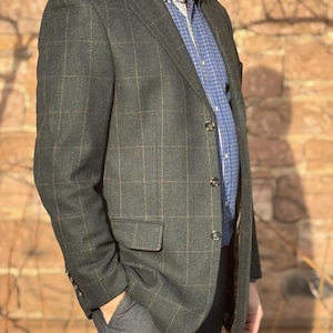 May include: A dark green blazer with a plaid pattern, paired with a blue checkered shirt and gray pants. The blazer has a classic three-button design and a pocket on the left side. The outfit is suitable for business or casual wear.