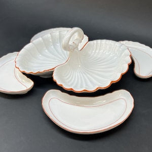 May include: A collection of white ceramic serving dishes, each with a seashell design and reddish-brown trim. The set includes dishes of various sizes and shapes, including one with a handle. Ideal for serving snacks or appetizers. The dishes are made of ceramic.