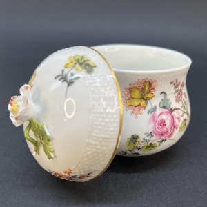 May include: A white porcelain sugar bowl with a lid. The bowl and lid are decorated with colorful floral patterns. The lid has a 3D floral accent.